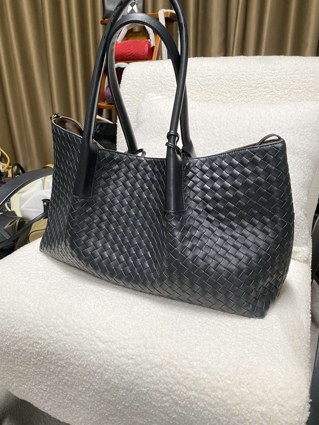 Logo-free top-grain cowhide woven tote — black front view on a white chair