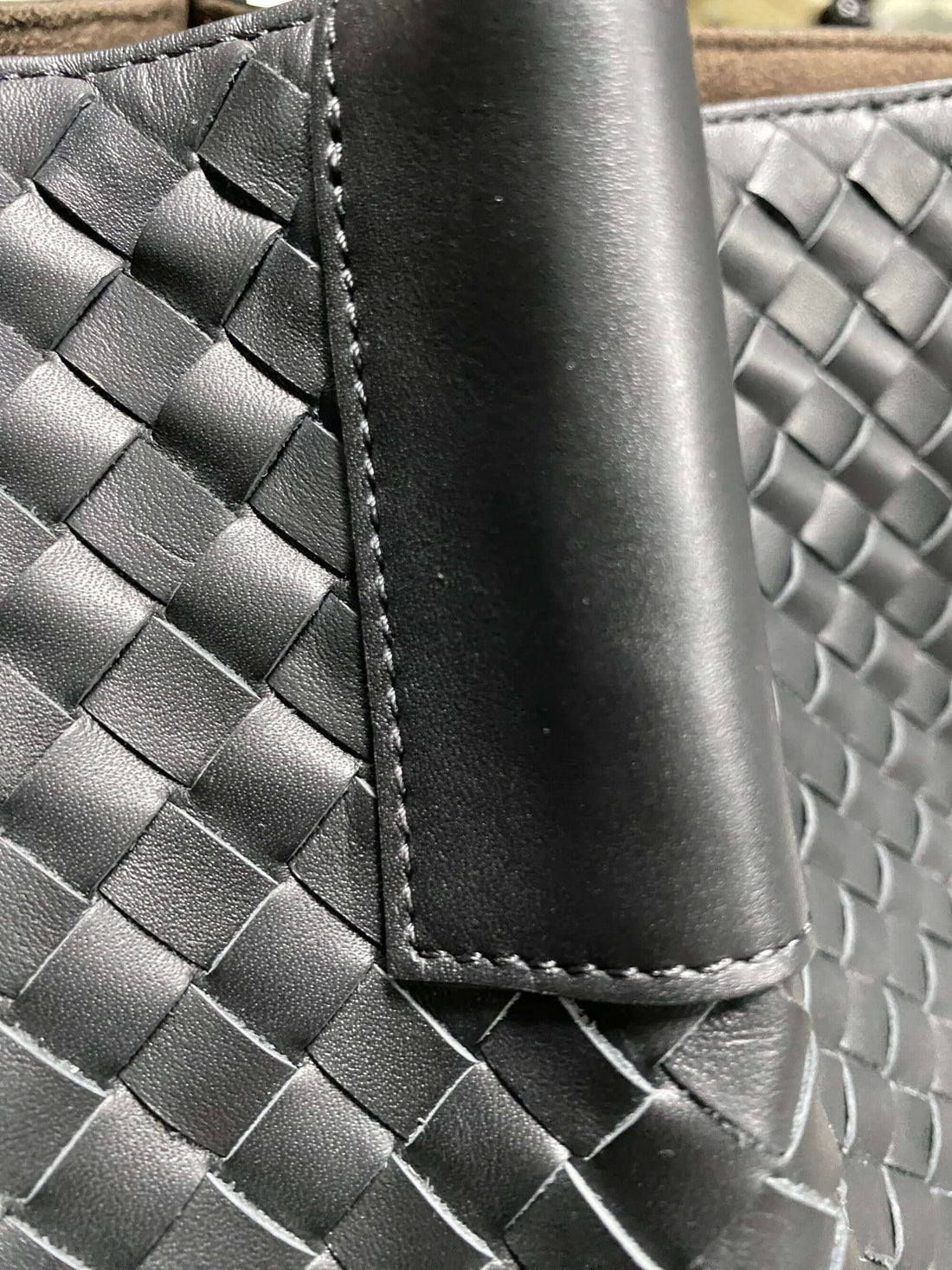 Logo-free top-grain cowhide woven tote — black handle stitching close-up