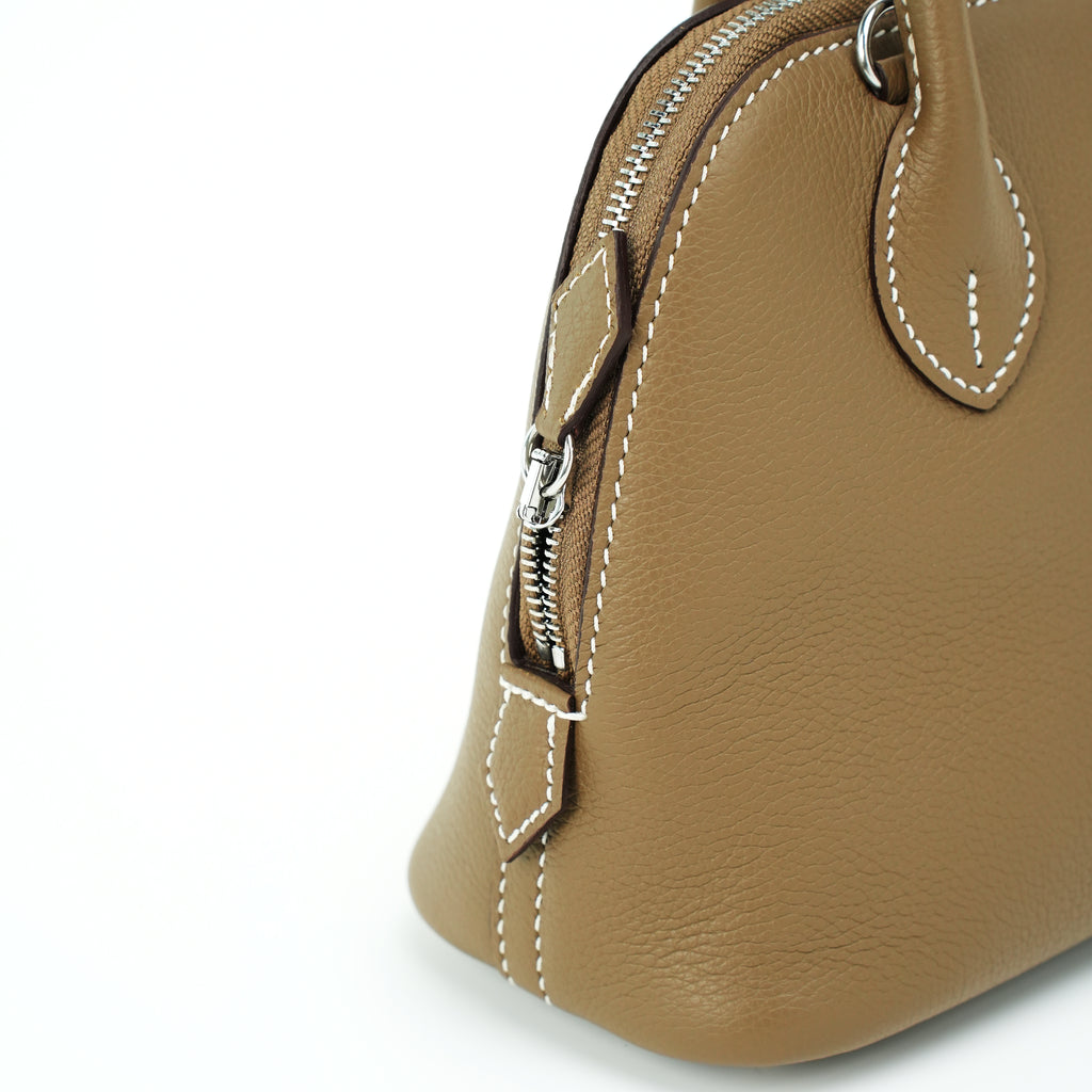 Side zipper and strap attachment on taupe leather dome handbag