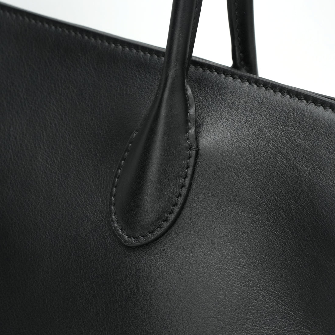 Logo-free full-grain cowhide shoulder tote — black handle stitching close-up