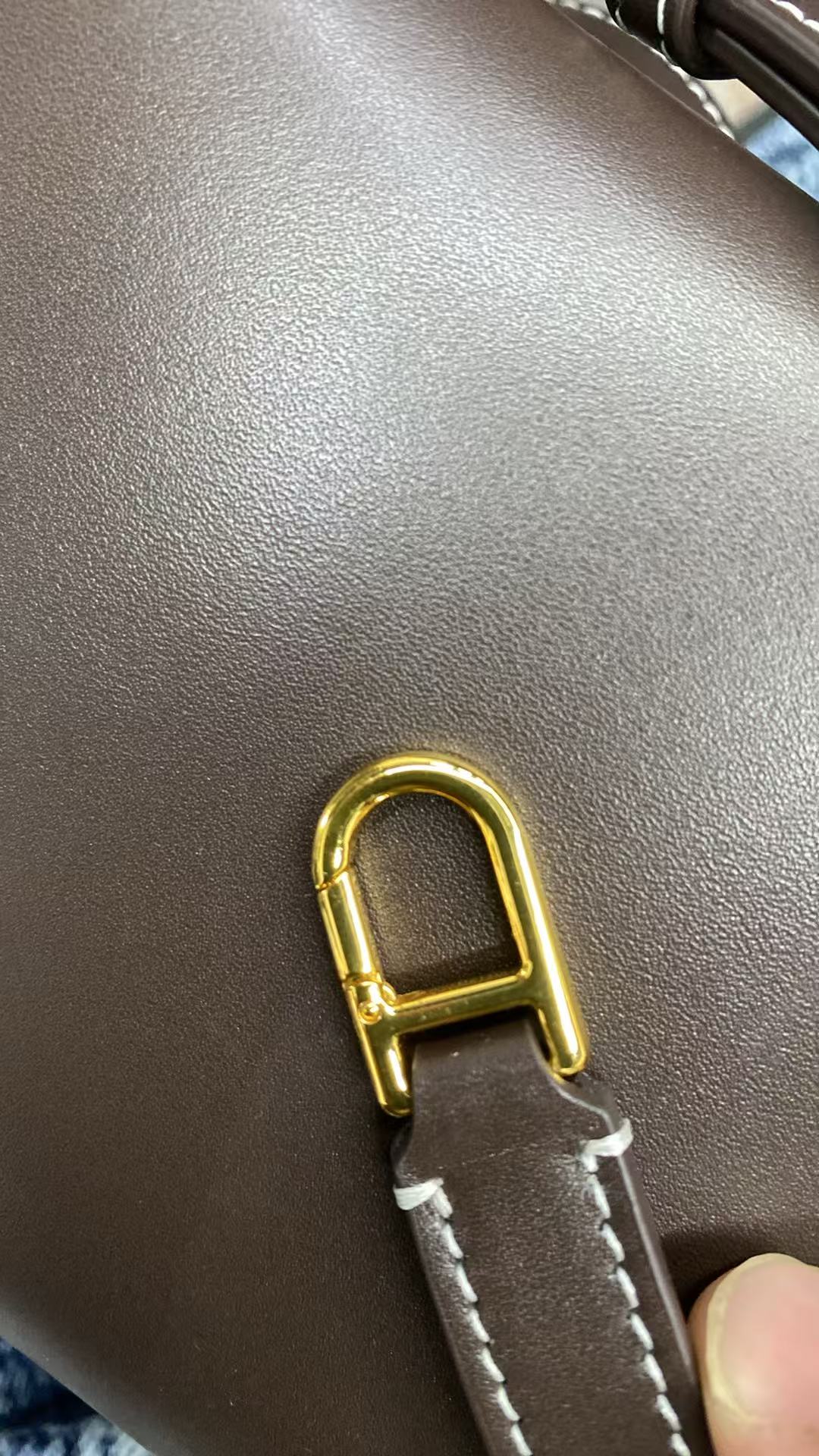 Gold-tone strap clasp on dark brown calfskin crossbody bag
