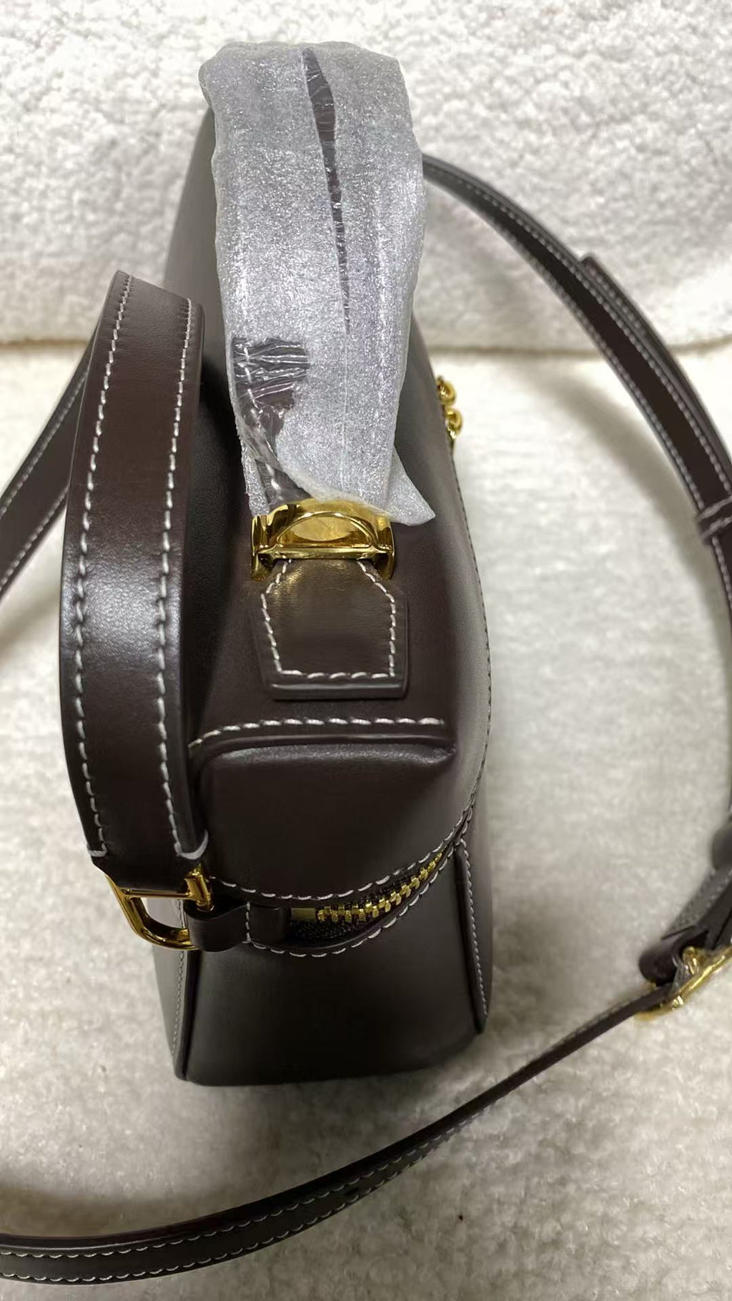 Dark brown calfskin box bag side profile with gold zipper and white contrast stitching