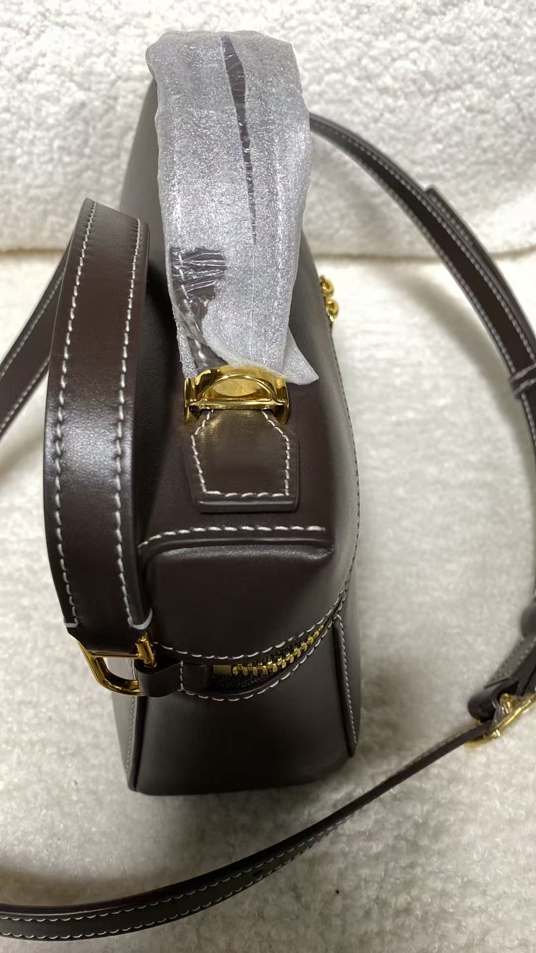 Dark brown calfskin box bag side profile with gold zipper and white contrast stitching