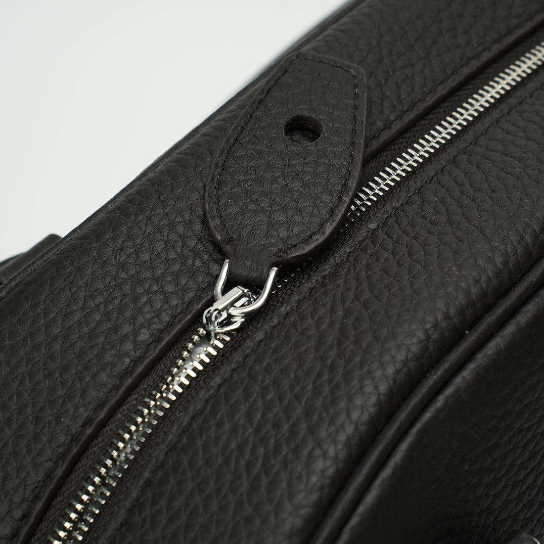Logo-free full-grain cowhide top-handle bag — silver zipper and closure tab close-up