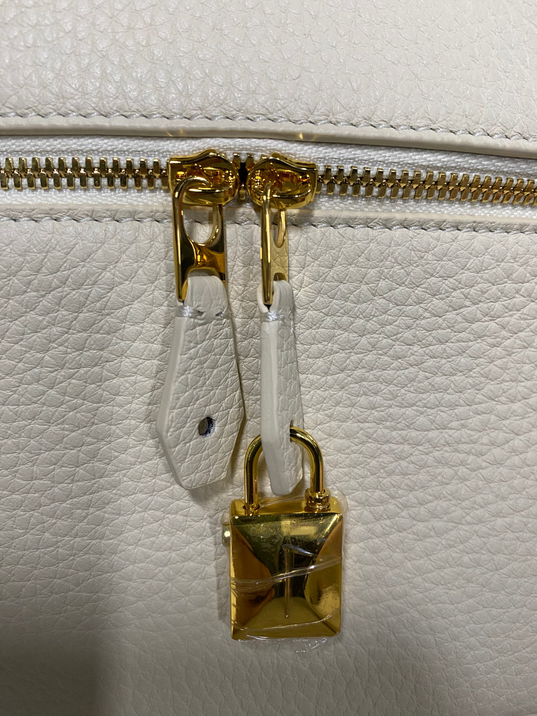 Gold double zipper pulls and padlock charm on cream leather vanity bag