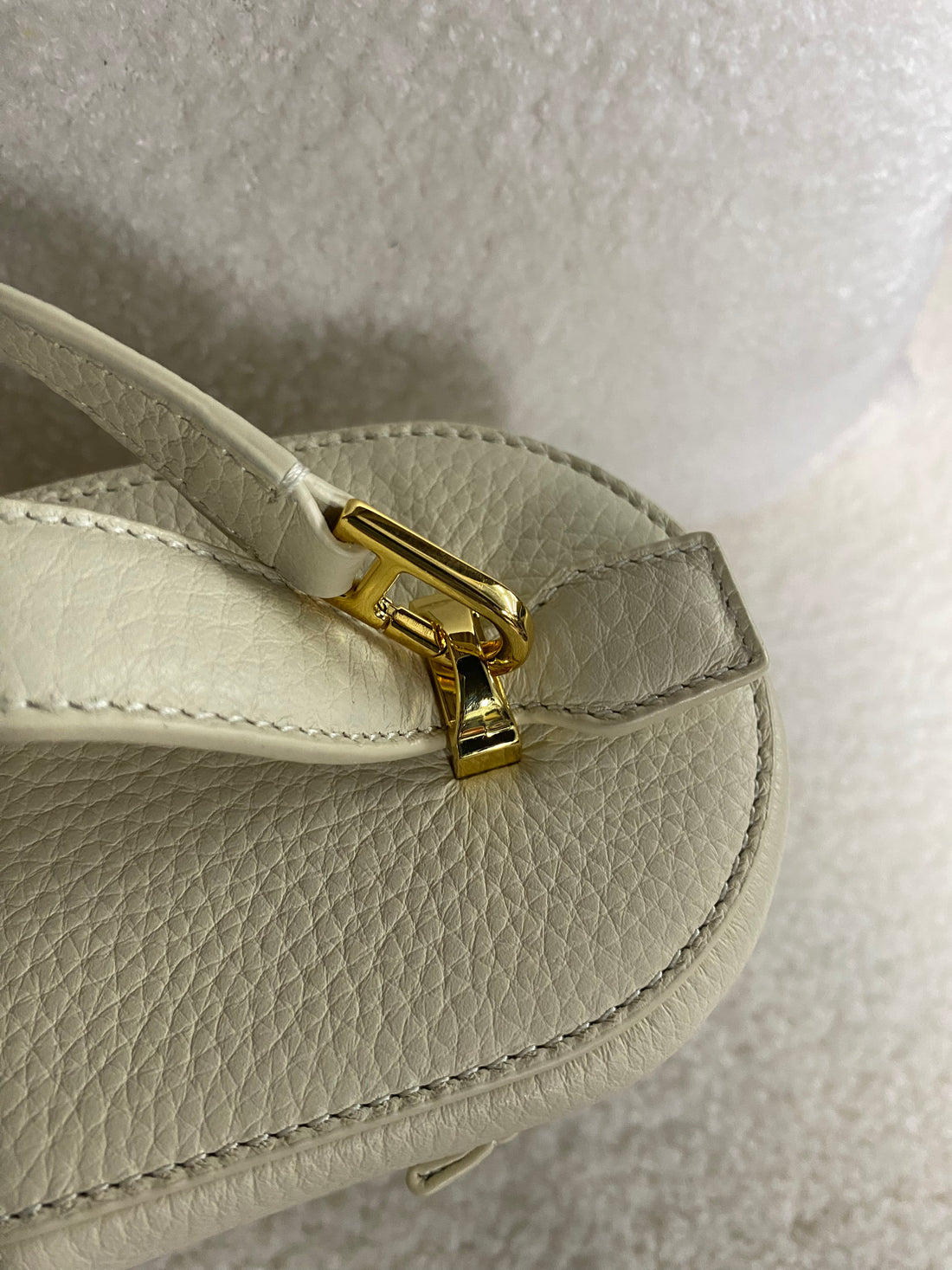 Gold crossbody strap clasp on cream pebbled leather bag