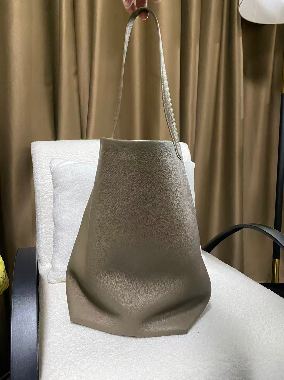 Taupe-grey pebbled cowhide bucket tote hanging by the shoulder strap