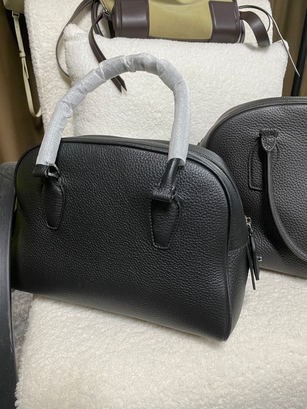 Logo-free full-grain cowhide top-handle bag — front view in a boutique