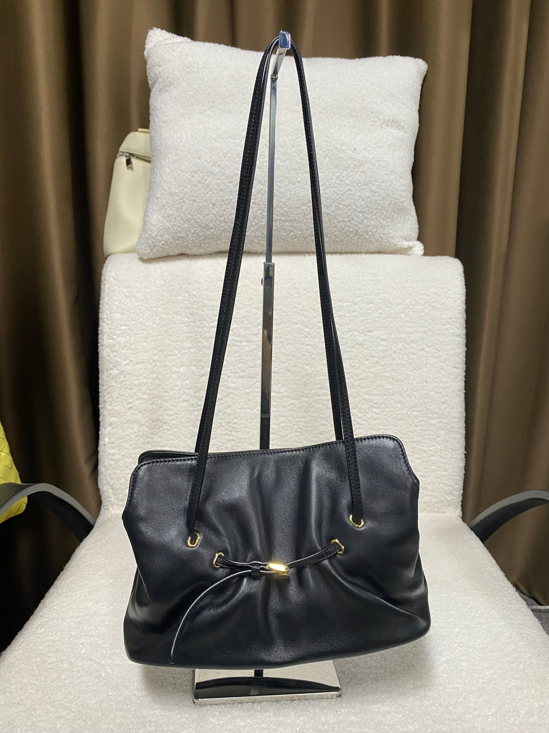 Black ruched lambskin crossbody bag — front view on a display stand
