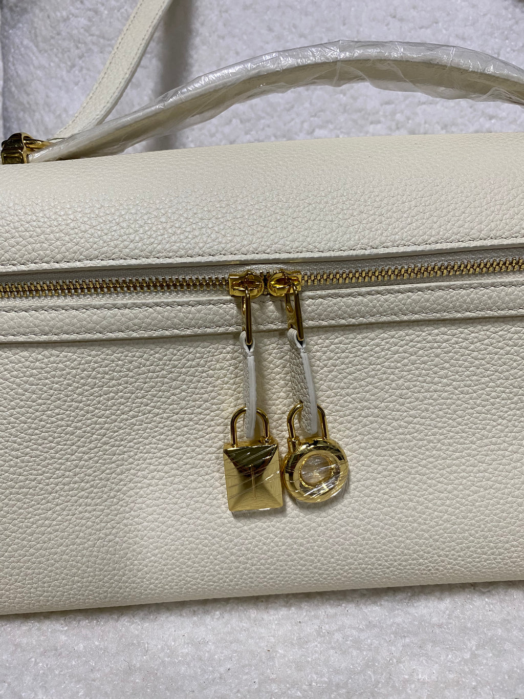 Gold zipper pulls and lock charms on cream white leather handbag
