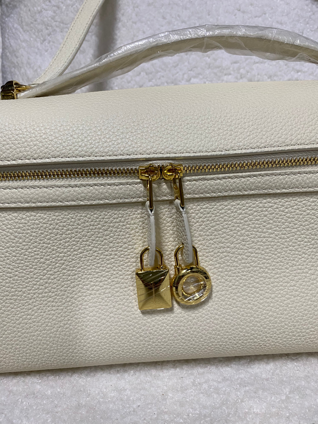 Gold zipper pulls and lock charms on cream white leather handbag