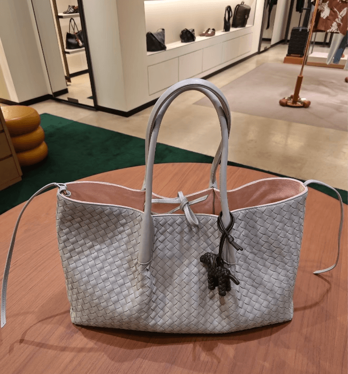 Logo-free top-grain cowhide woven tote — taupe grey front view in a boutique