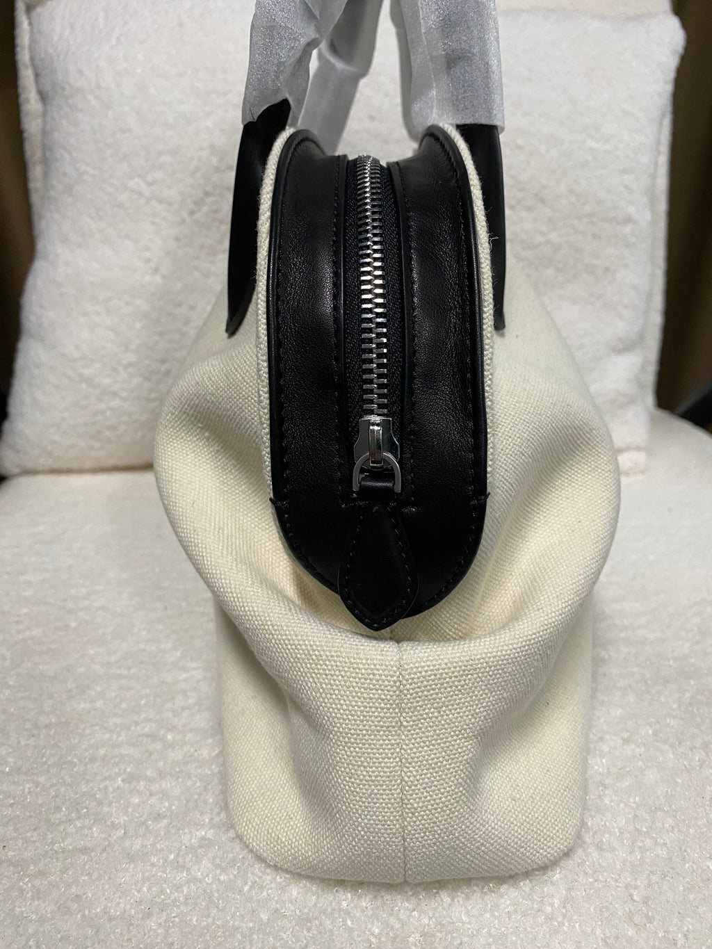 Side view of cream linen handbag with black zip-top closure