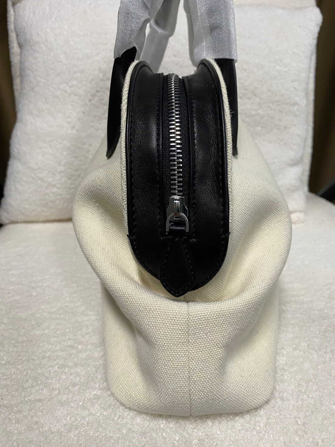 Side view of cream linen handbag with black zip-top closure