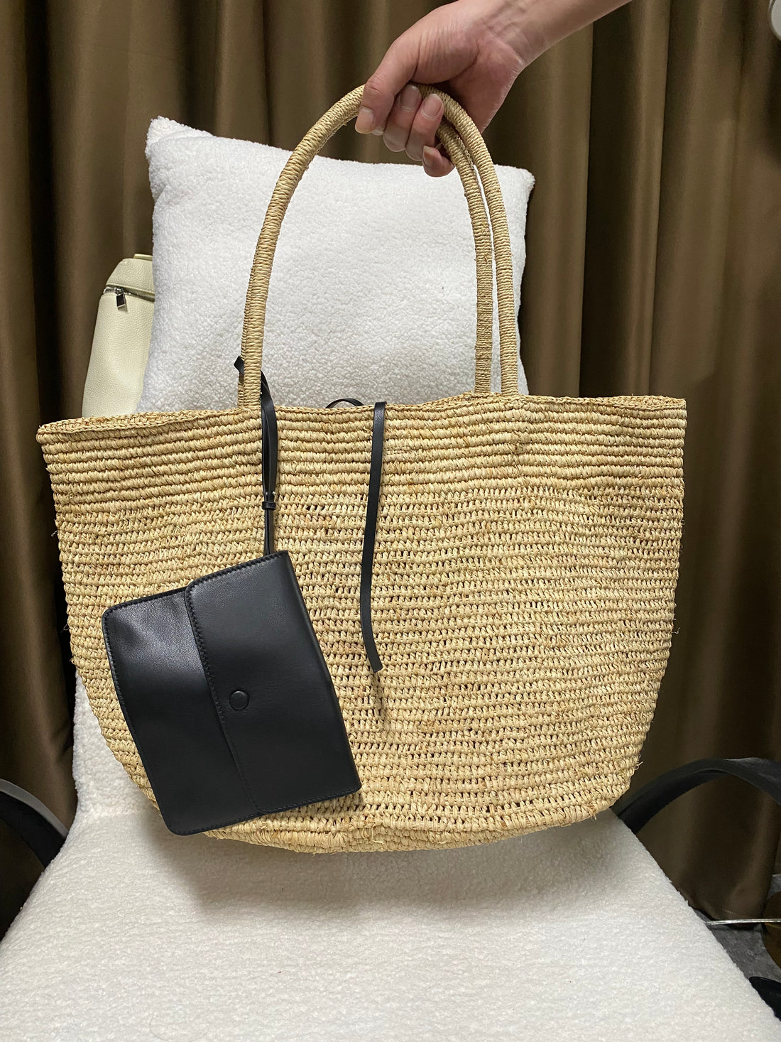 Beige natural raffia tote with black leather pouch held by the handles