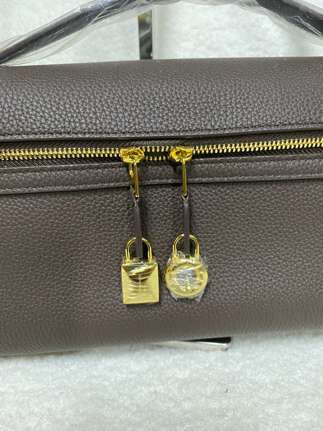 Gold double-lock zipper detail on coffee brown leather bag