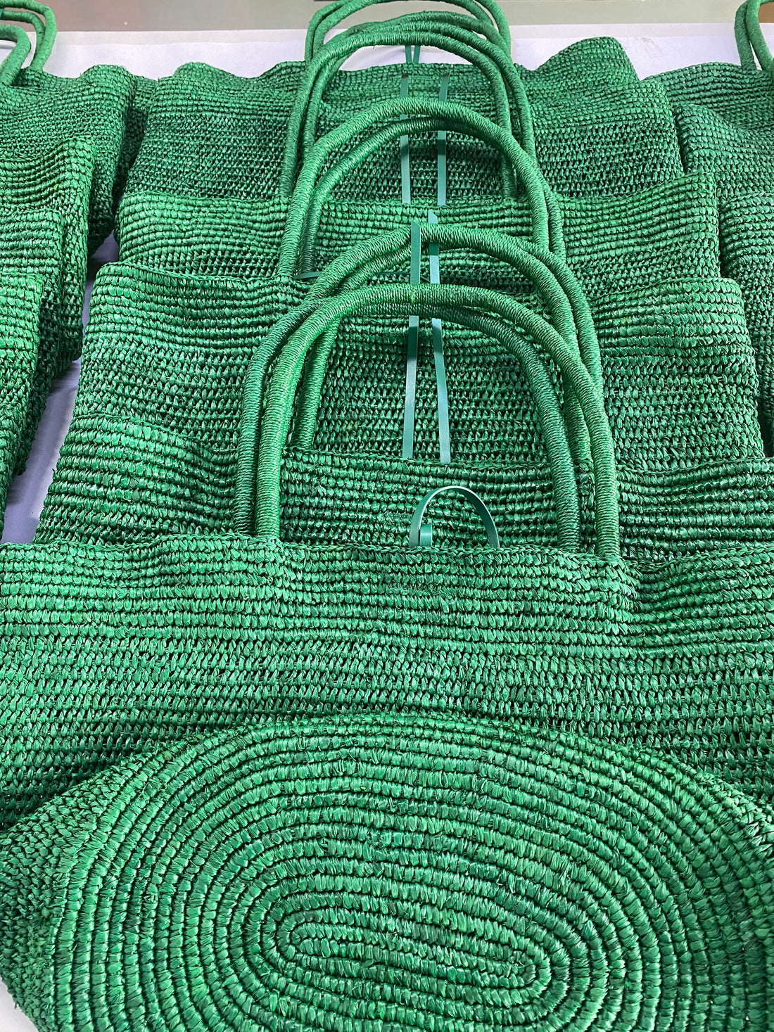 Emerald green raffia handles and leather pouch components during production