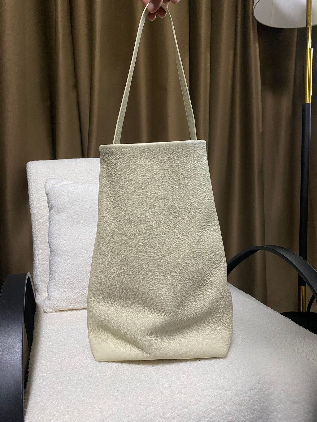 Cream full-grain cowhide bucket tote hanging from shoulder strap