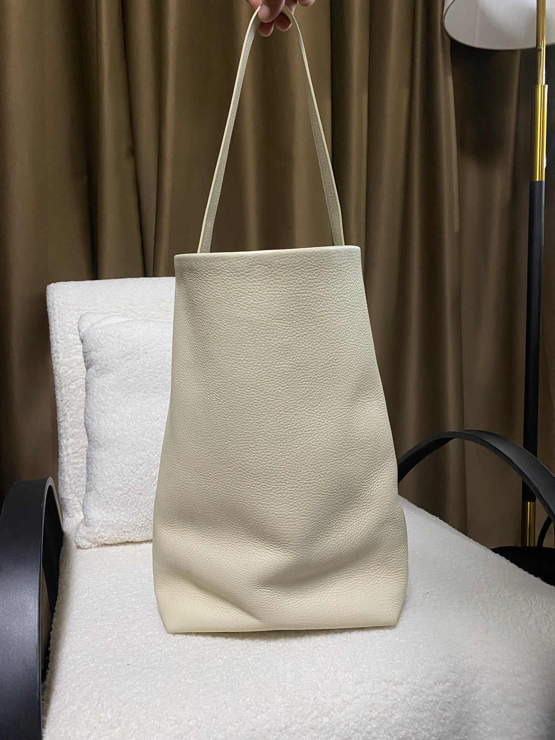 Cream full-grain cowhide bucket tote hanging from shoulder strap