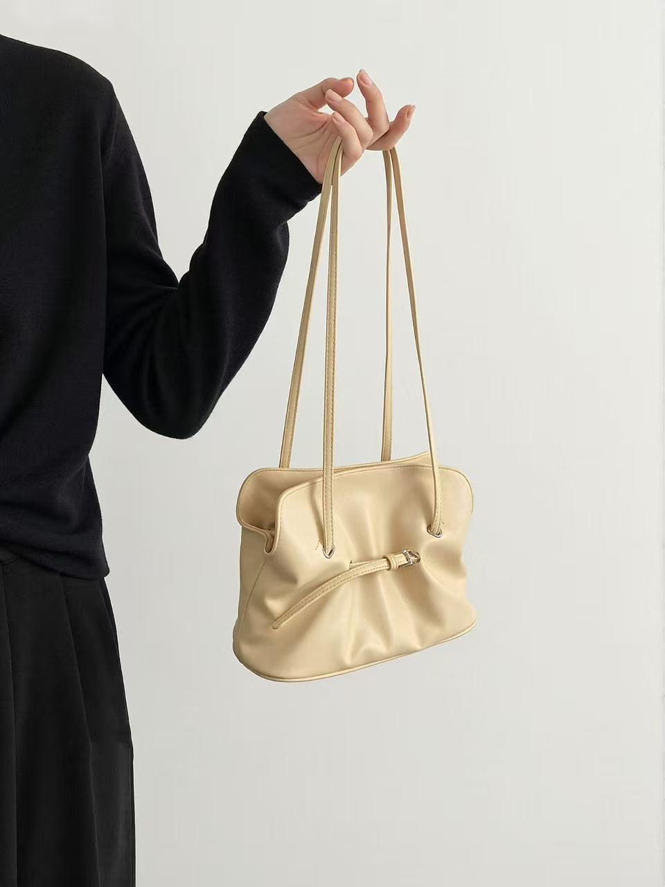 Black ruched lambskin crossbody bag — beige version held by a model