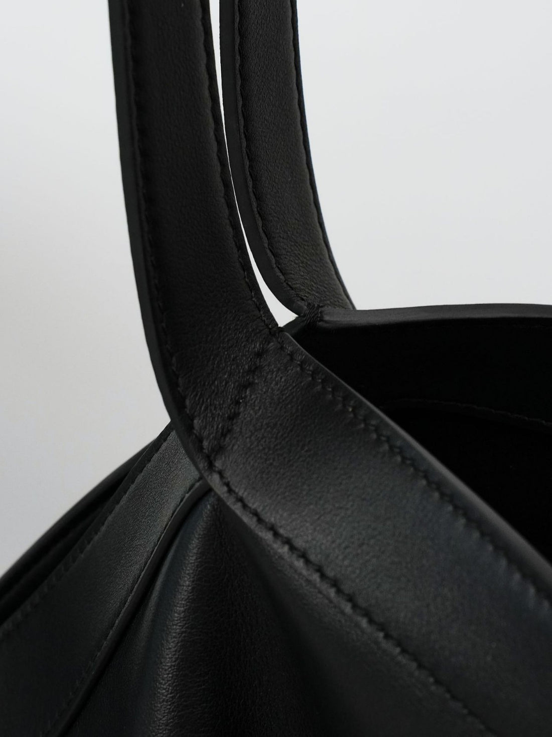 Logo-free black Y-strap slouchy leather tote — handle stitching close-up