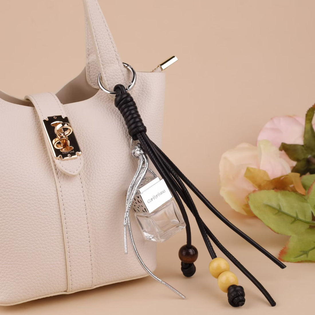 Black tassel perfume bottle bag charm attached to a white leather handbag