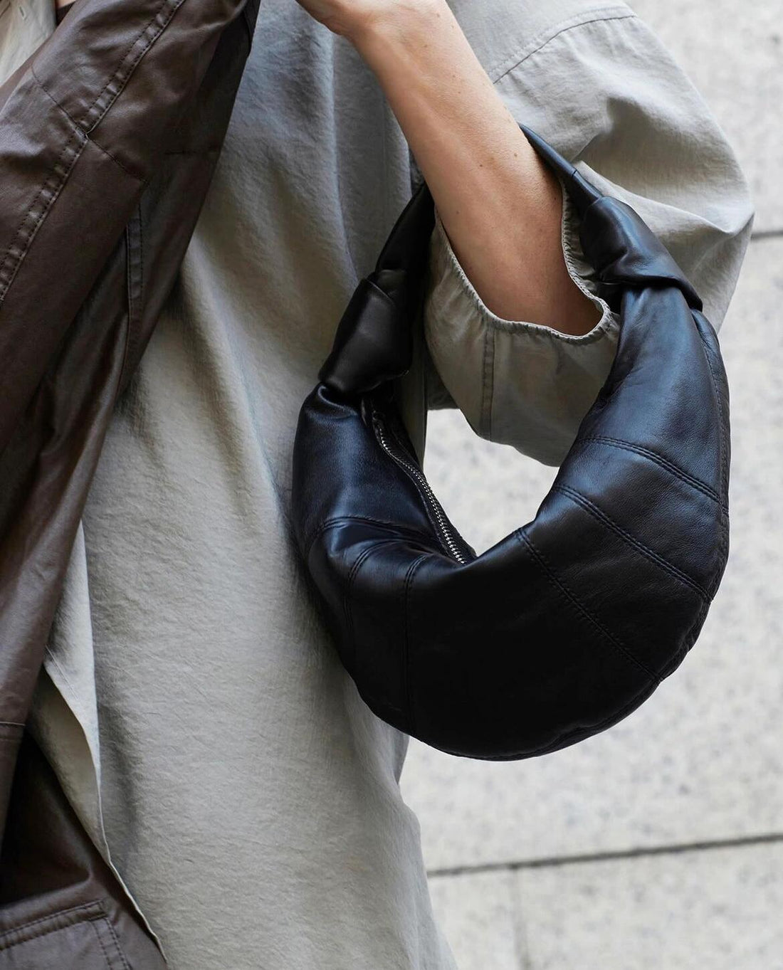 Logo-free lambskin croissant shoulder bag — black version worn under the arm