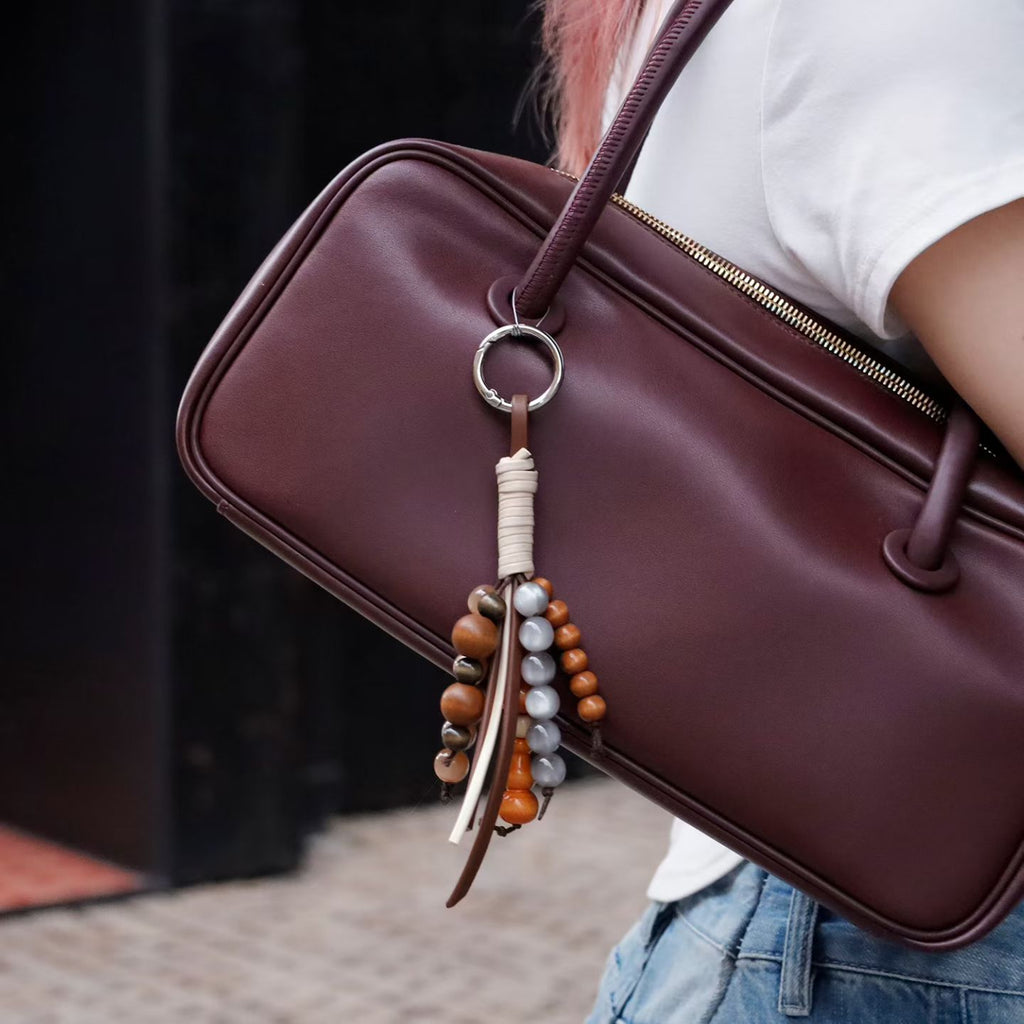 Mixed bead and tassel bag charm attached to a burgundy handbag