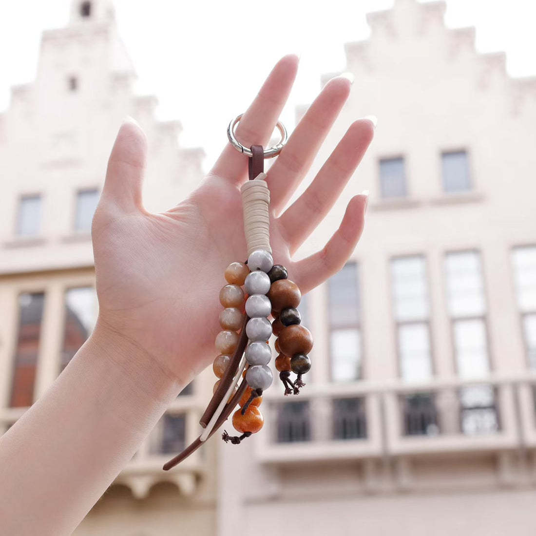 Hand holding a mixed wood and gray bead bag charm with leather-look tassels