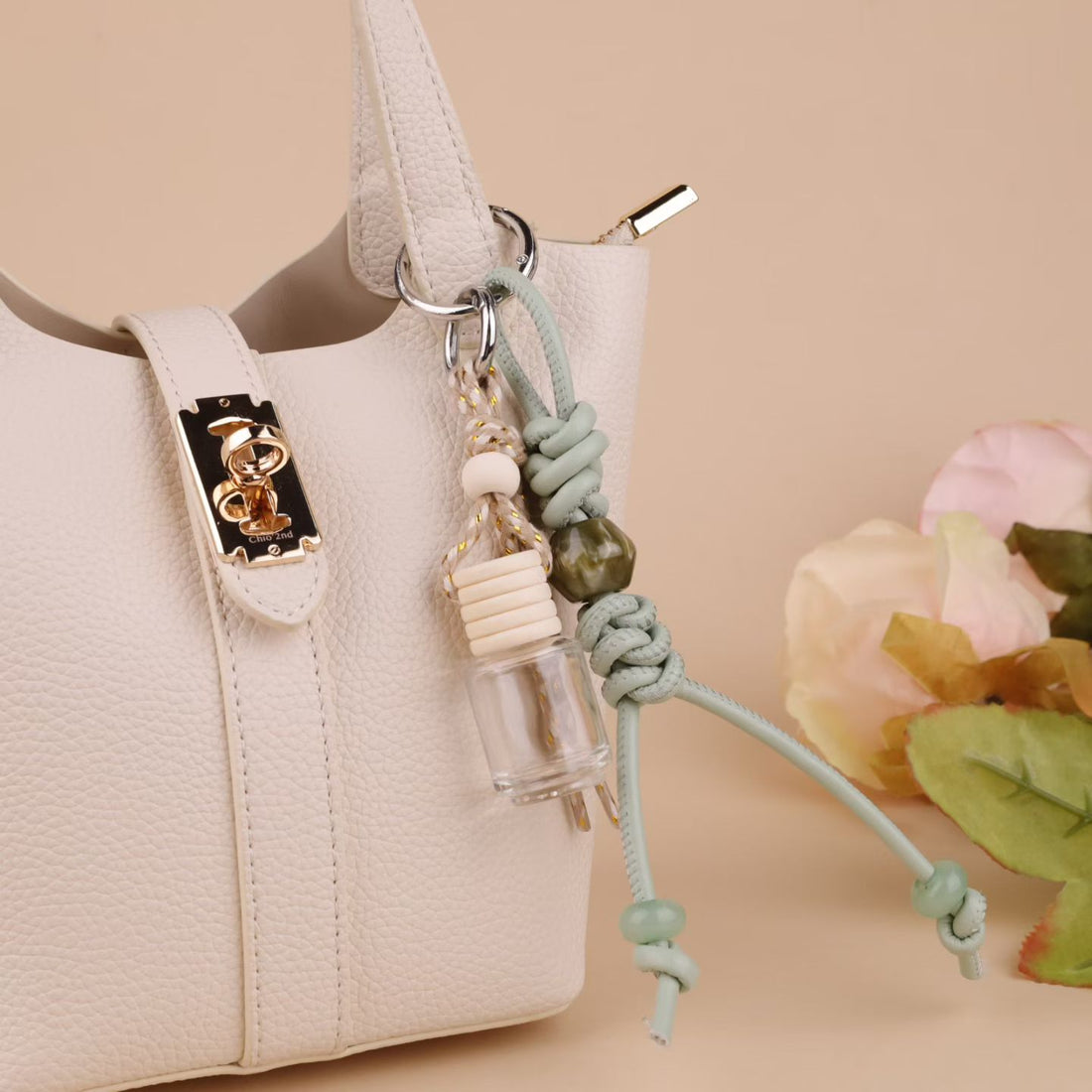 Sage green knotted rope glass bottle bag charm attached to a white handbag